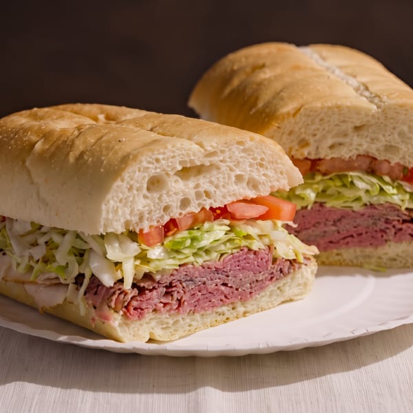 Two deli sandwiches on white bread with pastrami, shredded lettuce, and diced tomatoes.