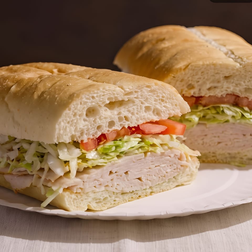 Two turkey subs with lettuce and tomato on a white paper plate.