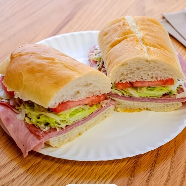 A large deli sub sandwich, cut in half, with meat, cheese, lettuce, and tomato on a white plate.